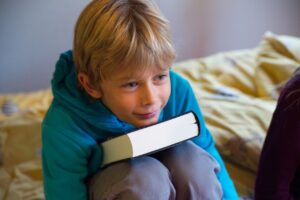 Philipp sitzt auf seinem Bett und stützt seinen Kopf auf ein dickes Buch ab.