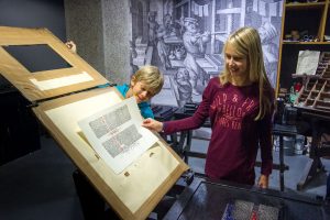 Ein Junge und ein Mädchen stehen im Guttenberg-Museum. Das Mädchen nimmt eine gedruckte Seite.