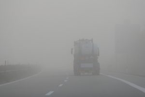 Nebel liegt auf einer Straße. Darauf fährt ein Lastwagen.