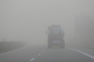 Nebel liegt auf einer Straße. Darauf fährt ein Lastwagen.