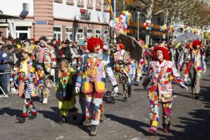 Ein Zug von Clowns zieht zum Karneval über die Straße.