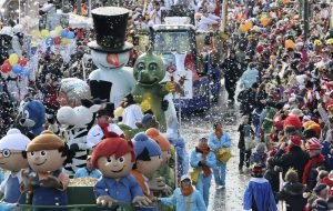 Ein Karnevalszug zieht durch eine Menschenmenge. Auf den Autos stehen einige Comicfiguren.