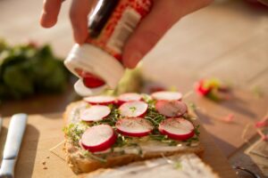 Ein Toast mit Kresse und Radisschenscheiben. Eine Hand würzt es mit Paprikapulver.