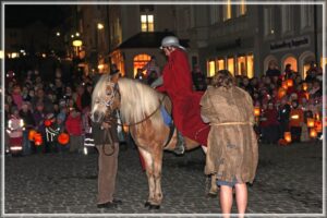 Ein Junge verkleidet als Sankt Martin sitzt auf einem Pony. Hinter ihm steht ein Sankt-Martins-Umzug.