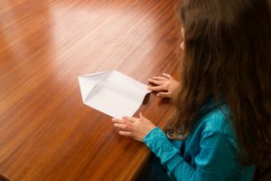 Ein Mädchen faltet die Ecke links oben von einem Blatt Papier.