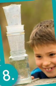 Ein Junge schaut auf einen Turm von vier übereinandergestapelten Plastikbecher. Ganz unten ist ein Glas.