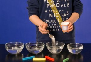 Ein Junge gibt Zucker in vier Glasschalen mit Wasser.
