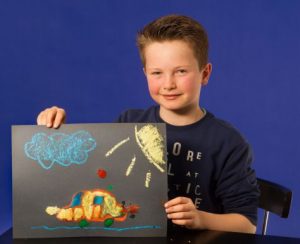 Ein Junge hält ein Bild hoch. Es wurde mit Zuckerkreide gemalt.