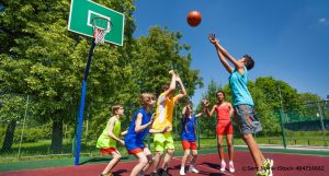 Eine Gruppe Kinder spielt Basketball, ein Junge will gerade einen Korb werfen.