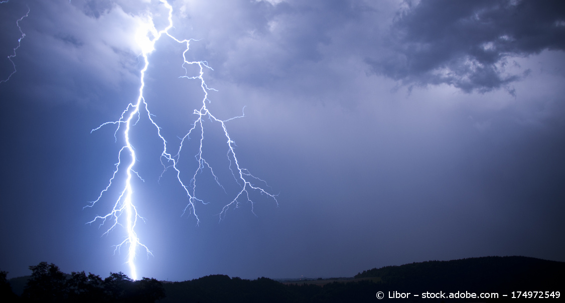 Ein Blitz schlägt neben Gewitterwolken ein.