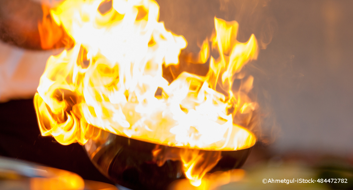 Eine Pfanne mit gelben Flammen. Sie lodern bis zur oberen Seite des Bildes auf.