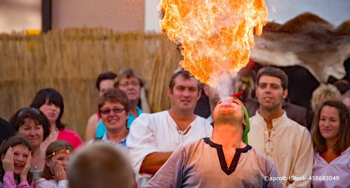 Eine Menschenmenge umringt einen Feuerspucker. Er ist dabei Feuer aus seinem Mund nach oben zu spucken.