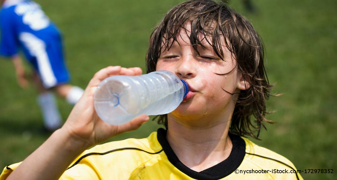 Ein Junge trinkt beim Fußballspielen aus einer kleinen Plastikflasche Wasser.