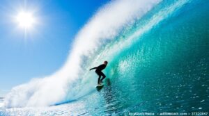 Ein Surfer reitet eine hohe Welle. Er trägt eine schwarzen Neoprenanzug.