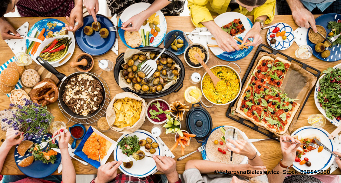 Ein Tisch mit vegetarischem Essen: Pizza, ein Couscoussalat, Brezeln, Hackfleischbällchen, Chips, Möhren, Oliven und Nudeln