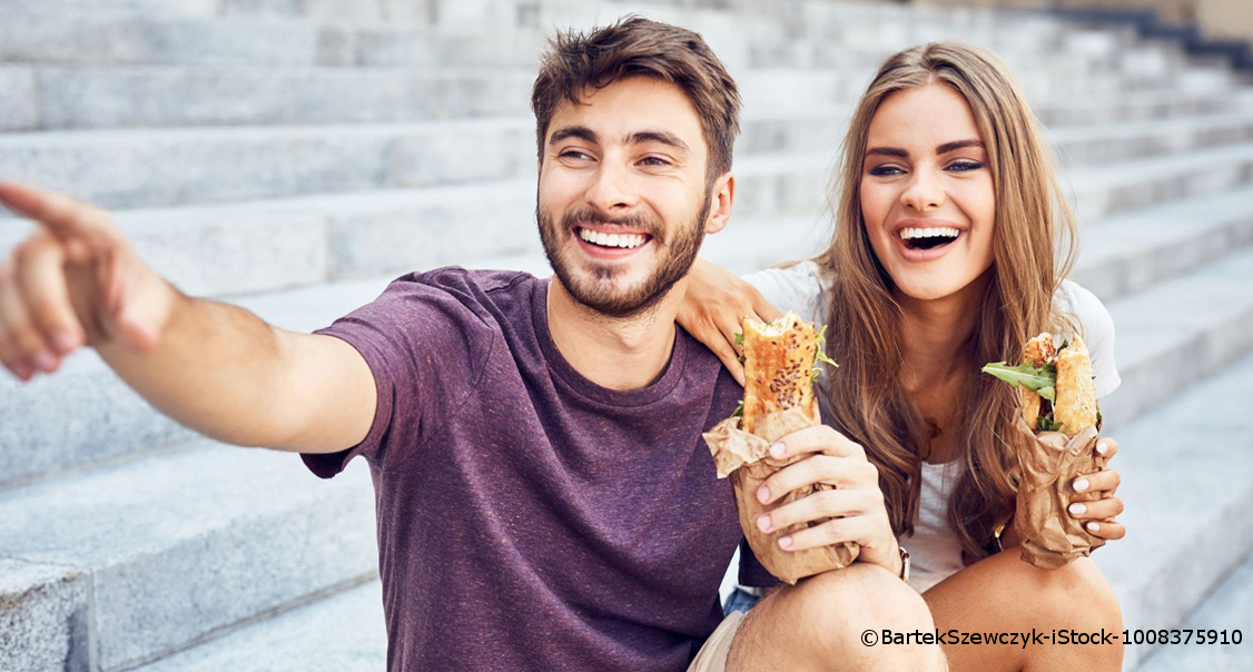 Ein junger Mann und eine junge Frau sitzen auf Steintreppen und halten beide Baguettes in den Händen.