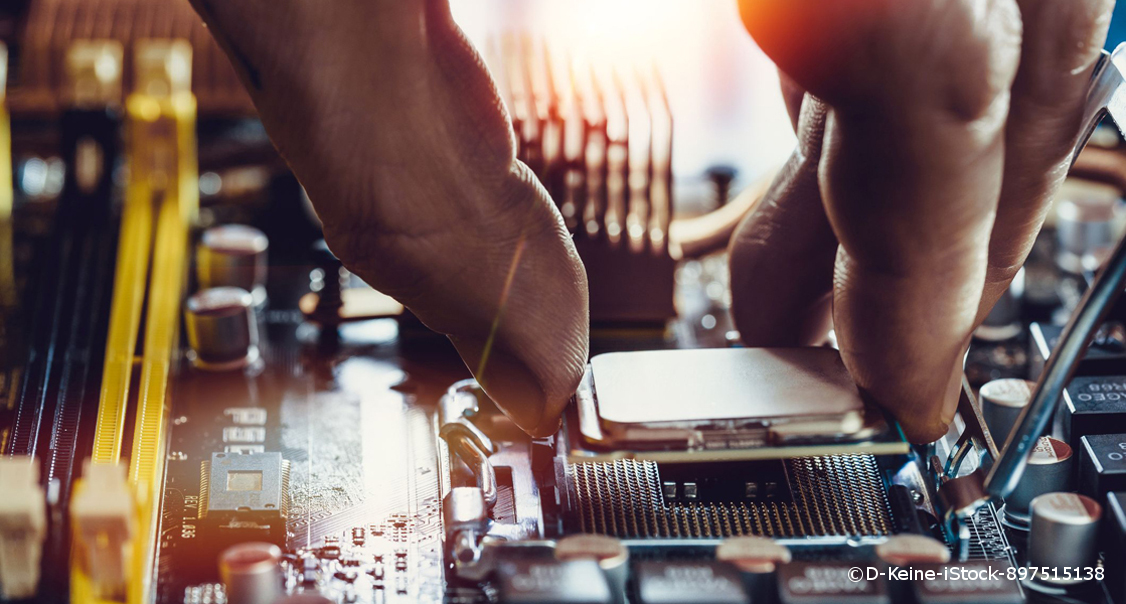 Ein Mensch rapariert einen Computer. Daumen, Zeige- und Mittelfinger halten einen Mikrochip. Er wird in eine kleine Apparatur eingepasst.