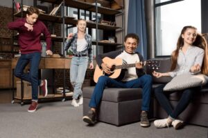 Eine Gruppe aus vier Kindern macht gemeinsam Musik. Ein Junge spielt Gitarre, ein Mädchen und ein Junge tanzen, ein weiteres Mädchen schnippst mit den Fingern.