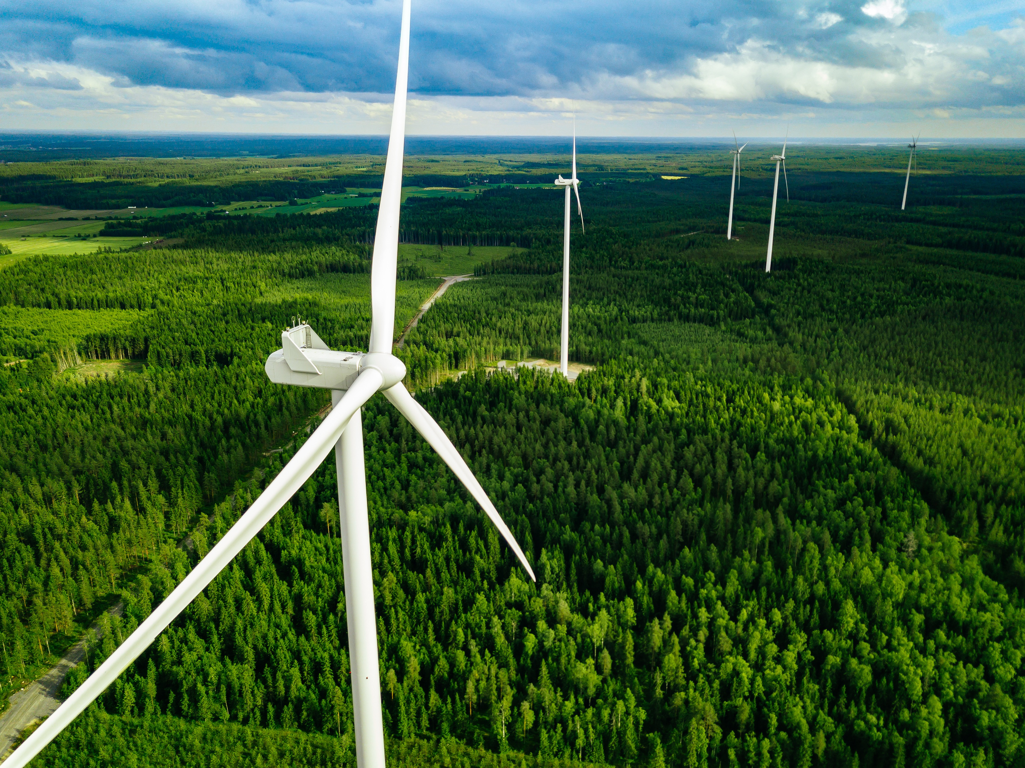 Windräder, die von oben fotographiert wurden. Zu sehen sind fünf Windräder, die alle nach Südosten ausgerichtet sind. Die Windräder stehen in einem Waldgebiet.