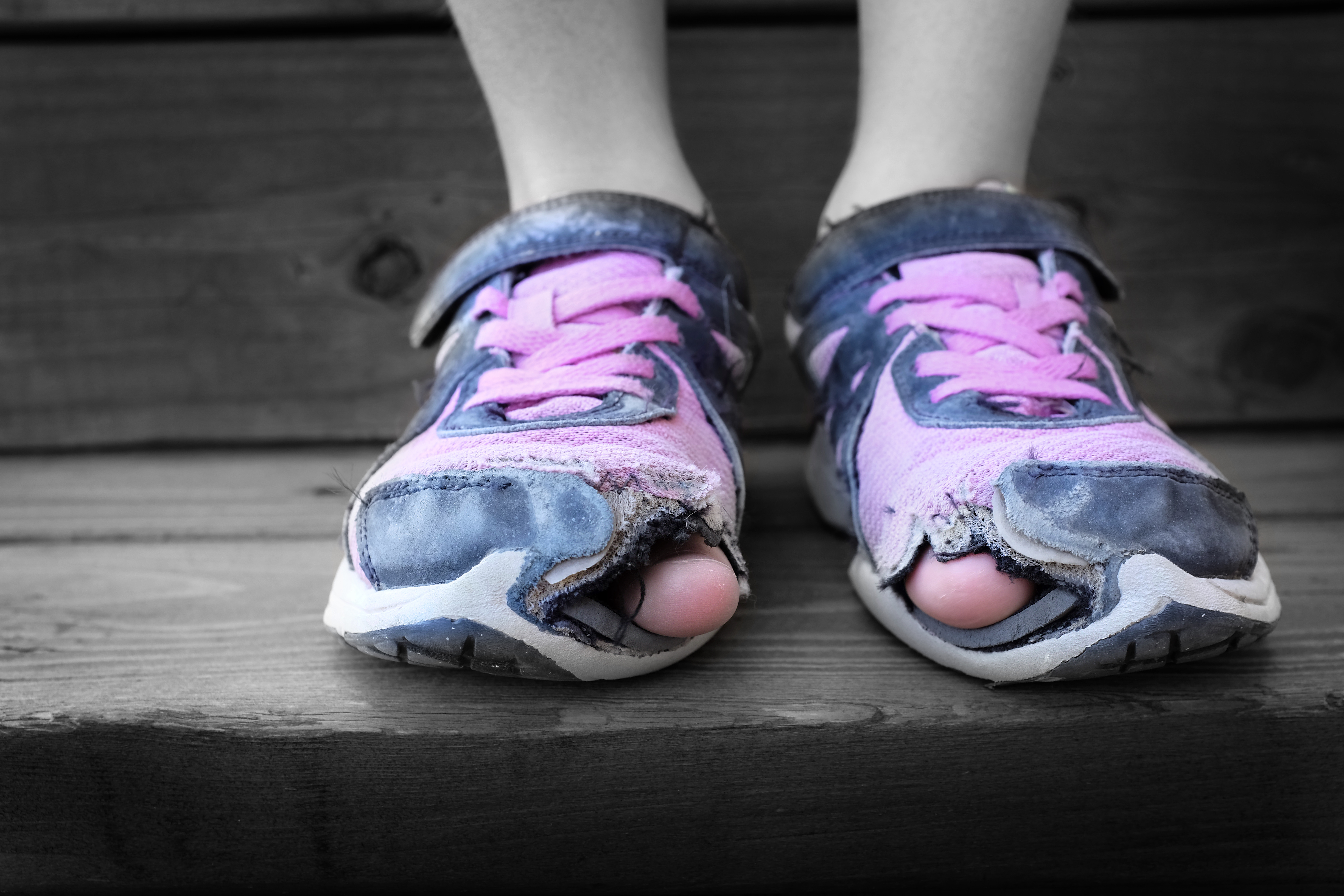 Ein Kind trägt alte Schuhe mit Löchern.