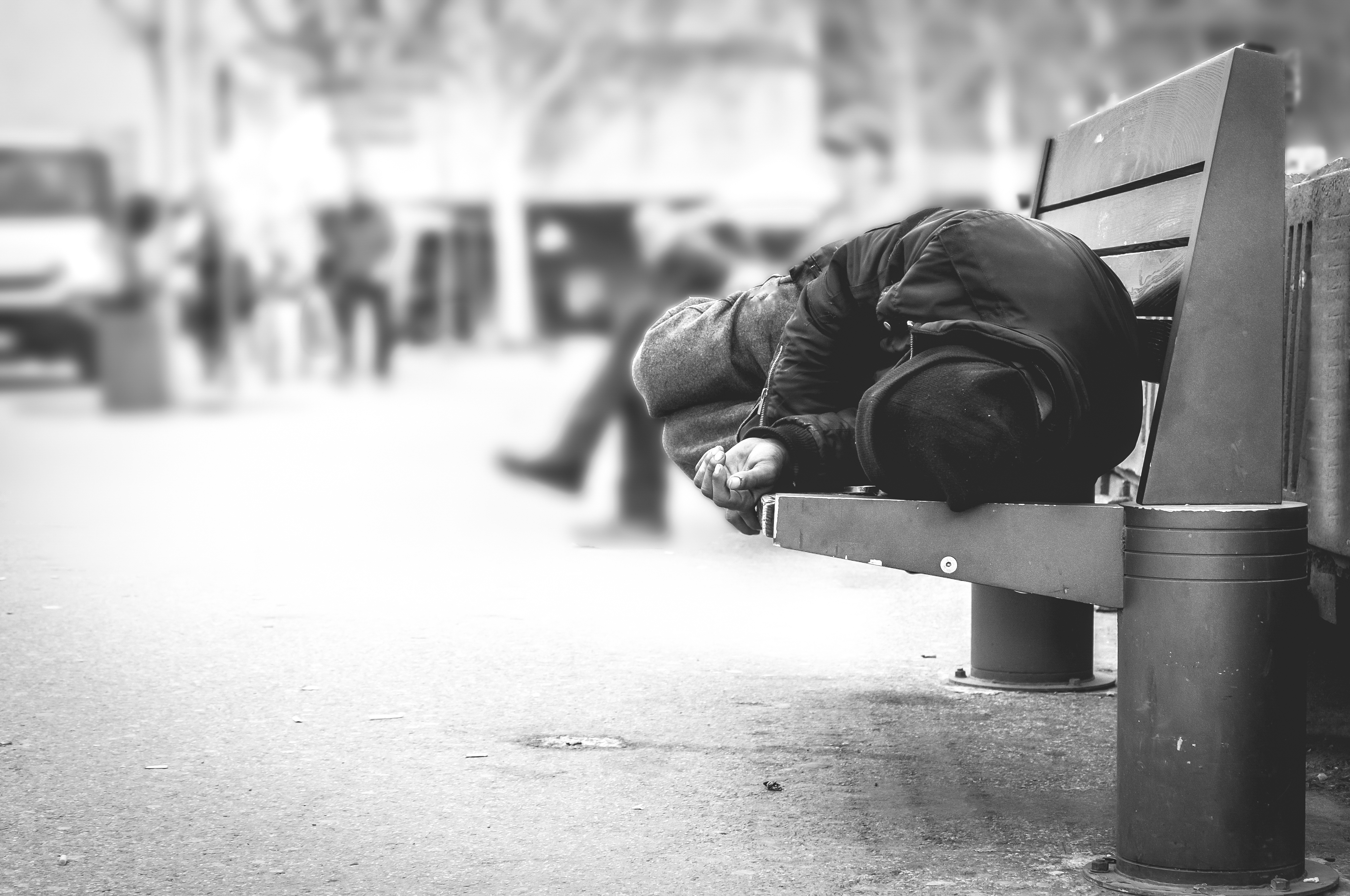 Ein von Armut betroffener, wohnungsloser Mann schläft auf einer Bank