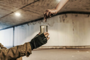 Eine Hand wirft Geld in den Becher einer wohnungslosen Person.