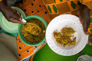 Welt ohne Hunger: Hände verteilen das Gericht Pilau auf einem Teller.